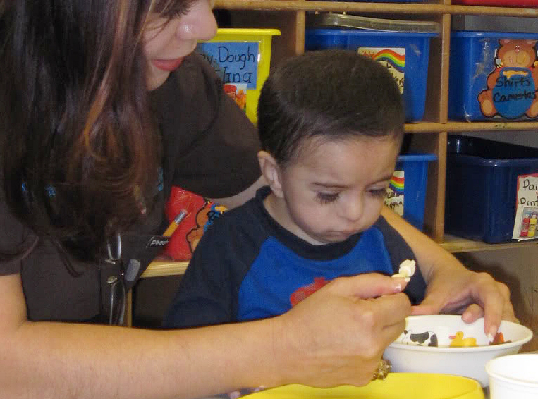 ECI staff helping toddler to eat