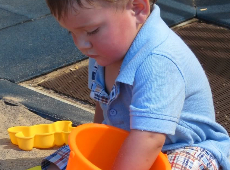 Toddler boy playing in sandbox with orange bucket