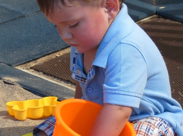 red-flags-toddler Toddler boy playing in sandbox with orange bucket