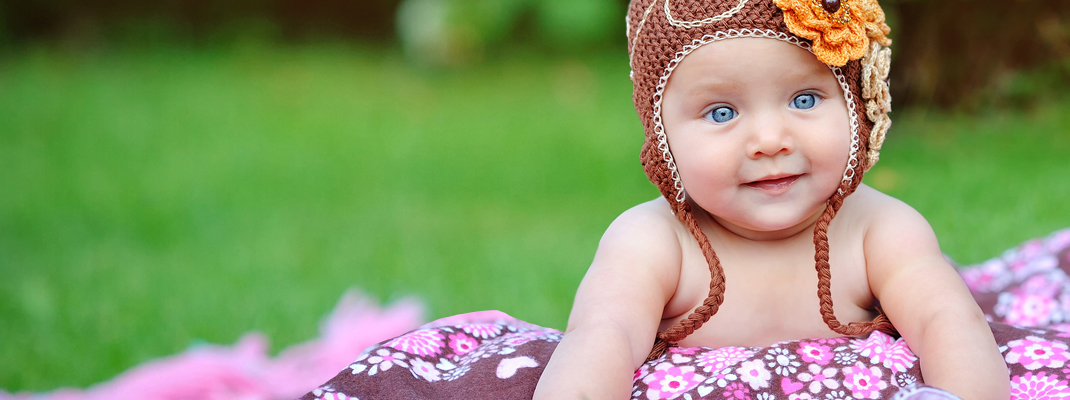 infant girl with flower hat sitting on blanket outdoors